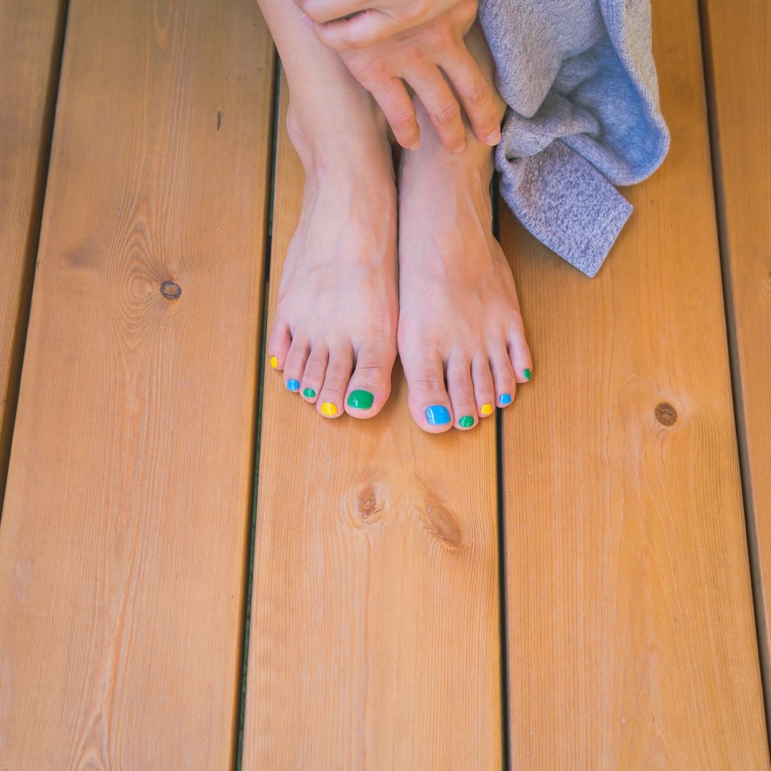 Bare feet with blue, green, and yellow toenails on wooden planks.